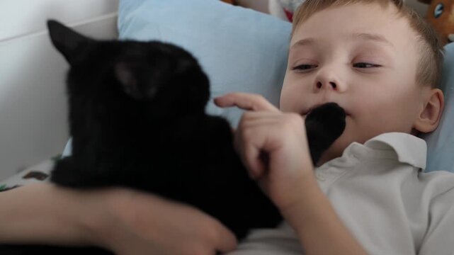 Happy little boy relaxing at home while cuddling his black cat. Warm, cozy family moment showing love, friendship and trust between child and pet.
