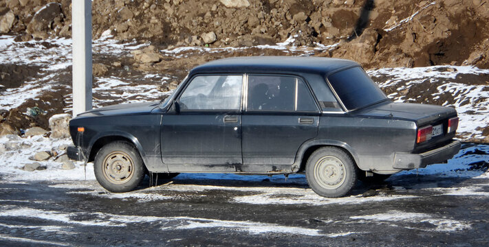 Kazakhstan, Ust-Kamenogorsk february 28 2025: Black VAZ 2107 sedan parked near freshly dug soil piles. Soviet car on dirty construction ground, urban outdoor scene with slush and earthworks background