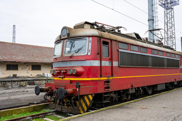 Obraz premium a vintage red electric locomotive leading a line of train cars along a concrete station platform.