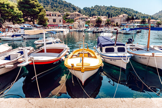 View of boats bobbing gently on the turquoise water, reflecting the quaint buildings nestled against the verdant hills under a clear sky, Lopud, Dubrovnik-Neretva County, Croatia.