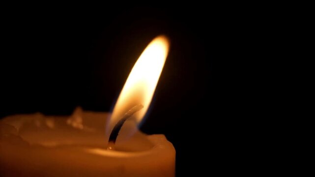 Soft flame dancing above a white candle against a dark black backdrop, capturing quiet light and dramatic silhouette in a close‑up view