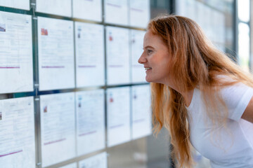Fototapeta premium Woman looks closely at a bulletin board with various notices and information in a modern building