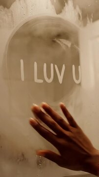 Close-up of a hand writing "I Luv U" on a steamy bathroom mirror, creating a romantic and intimate moment