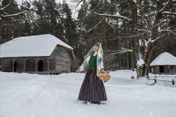 Latvian woman in traditional dress poses in a village in winter. Riga, Latvia.