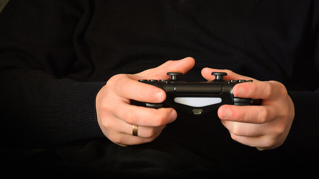 Close up of male hands holding a black wireless gamepad while playing video games at home