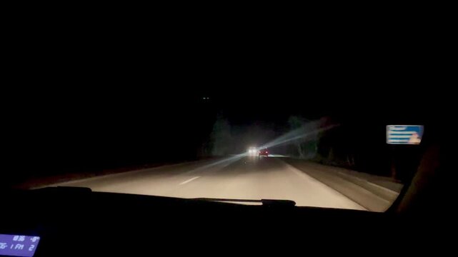 Night driving on a suburban highway with oncoming car headlights and dark forest background