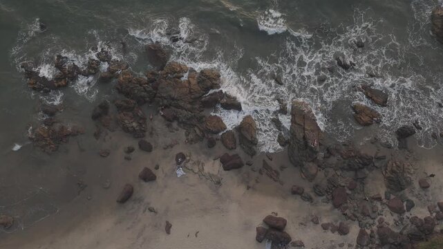 Top-down aerial close-up of Arambol Beach, Goa, with soft winter light illuminating golden sand, textured rocks, and gentle waves moving along a calm Arabian Sea shoreline