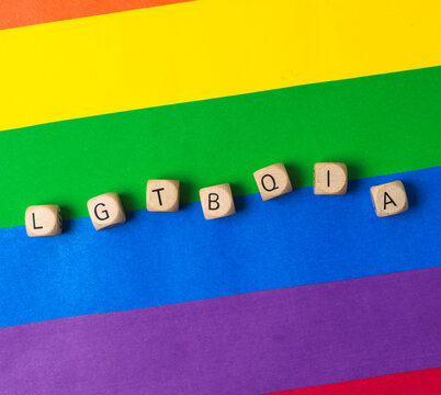 Wooden dice forming the letters lgbtqia plus on a colorful rainbow pride flag