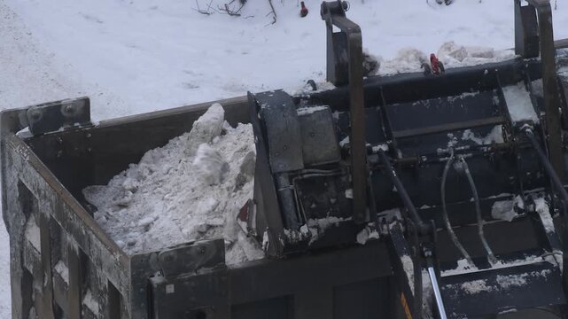 A front loader loads dirty snow into the bed of a dump truck. City utilities clean up the streets after a heavy winter snowfall