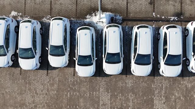 Aerial view of multiple new white cars parked in a straight line on a snow-covered parking lot at a car dealership, commercial auto showroom display, brand new vehicles for sale, modern automotive ret