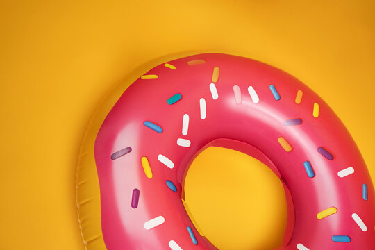 Top view of a pink donutshaped pool float with sprinkles on a vibrant yellow backdrop