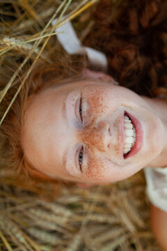 Smiling with red hair and freckles lying in wheat field wearing white dress