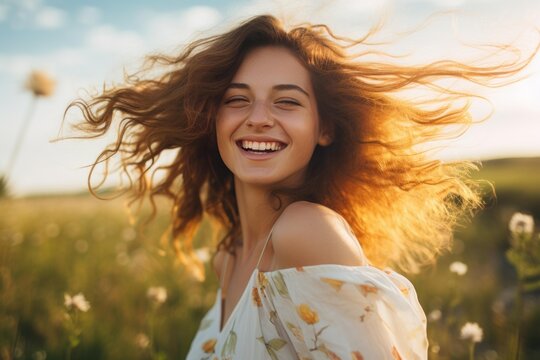 Young woman laughing happily in a sunny meadow with her hair blowing in the wind