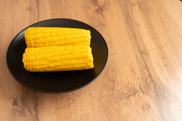 Boiled corn on black plate on wooden table in minimal style  