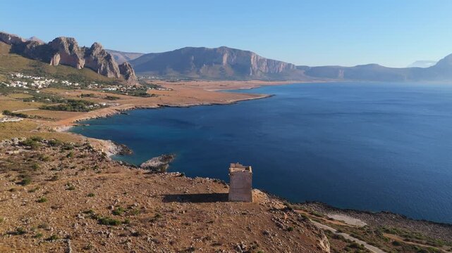 Zoom out drone view of Torre Isulidda in Sicily showing coastal cliffs, open sea and mountain landscape under clear skies.