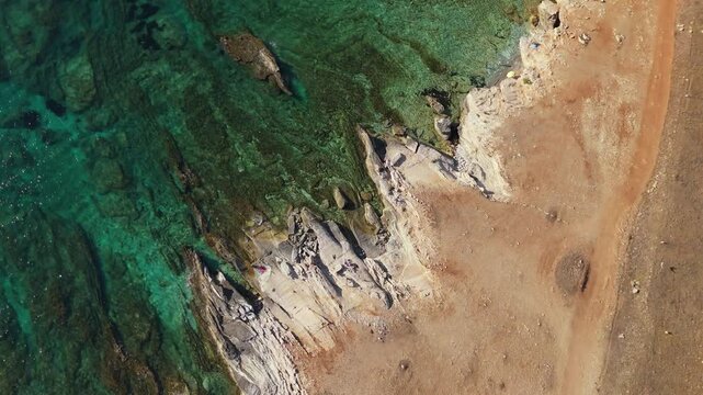 Zenithal spiral zoom in over a Sicilian beach with rocky formations and crystal clear turquoise water, revealing textures and shoreline patterns from above.