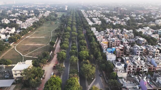 Wide aerial shot of Greater Noida highlighting planned housing blocks, community green space, and surrounding greenery, softened by atmospheric haze that reveals ongoing urban expansion.