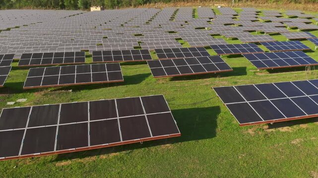 Aerial tilt-up over over large-scale solar panel array installed on green grassy field in rural countryside.