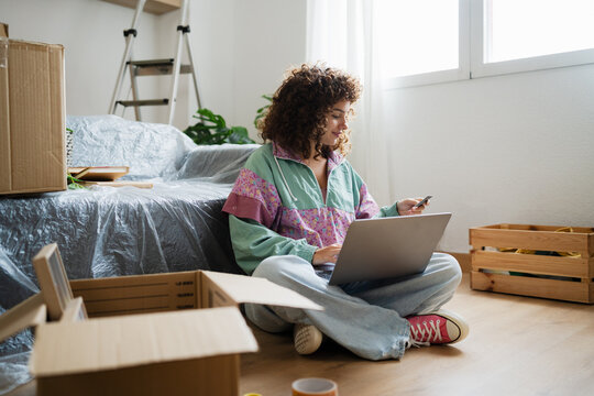 Woman making online payment with laptop at home surrounded by boxes