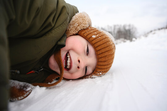 Smiling child lying in snow wearing warm clothes and ear flap hat