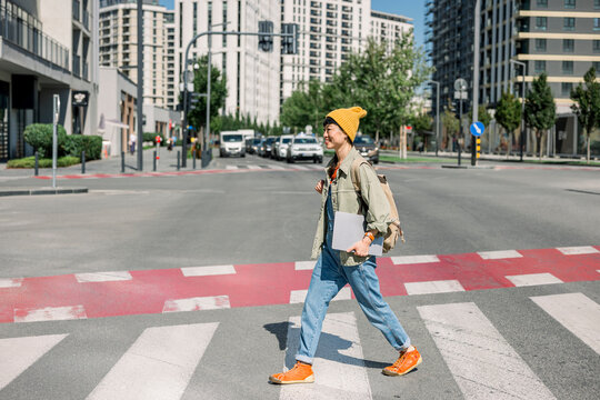 Woman walking in city with laptop and backpack in casual outfit