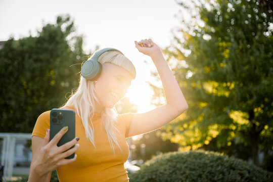 Woman dancing outdoors with headphones and mobile phone in sunlight
