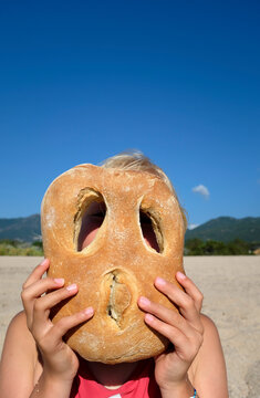 Person holding bread with face holes on a beach in Corsica