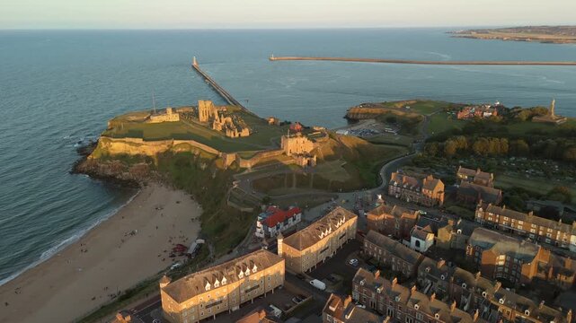 Sunset casts a warm glow over Tynemouth Pier along the North Sea at dusk. Aerial drone footage