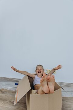 Child sitting in cardboard box with arms raised during moving day