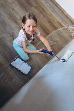 Smiling child painting a wall with a roller during home renovation