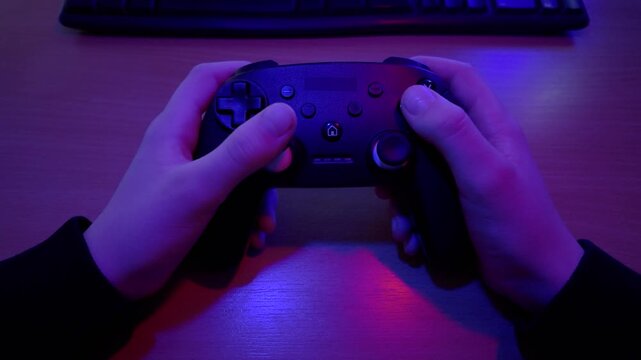Hands holding game controller while playing video game, close up view with purple lighting and focused gaming atmosphere