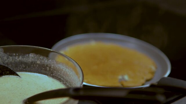 Close up of a thin pancake or crepe cooking on a hot griddle with steam rising, featuring a bowl of fresh batter in the foreground. Ideal for cooking tutorials and breakfast concepts.
