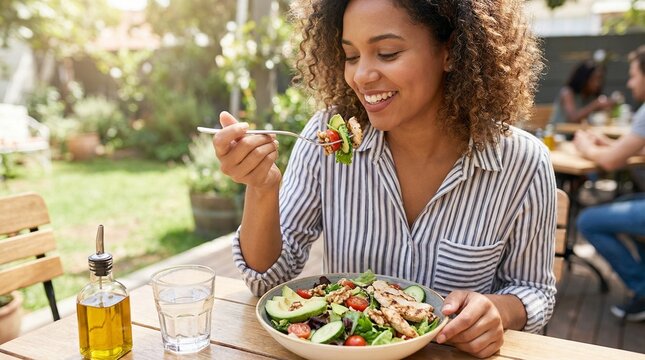 Young Black woman eating fresh salad at outdoor cafe, healthy lunch and mindful nutrition, cheerful lifestyle moment in summer light, wellness and diet choice