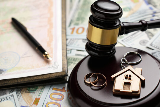 Property Division in Divorce and Marital Law Concept. Gold wedding rings, wooden house model, and a judge gavel on legal paperwork and US currency. Division, alimony, and real estate legal disputes