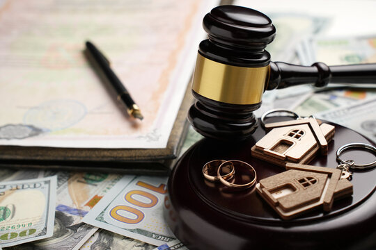 Property Division in Divorce and Marital Law Concept. Gold wedding rings, wooden house model, and a judge gavel on legal paperwork and US currency. Division, alimony, and real estate legal disputes