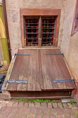 Weathered wooden cellar door beneath a barred window on an old Colmar facade.