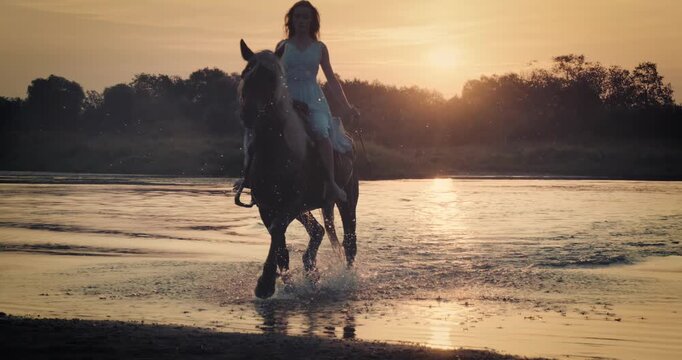 Super slow-motion footage of a rider galloping on horseback through shallow river at sunset. Dramatic splashes and warm golden light create a cinematic outdoor adventure scene.