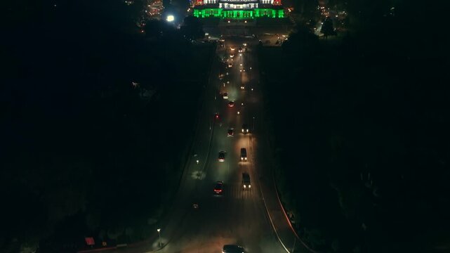 Aerial view of a building illuminated with vibrant lights, with a road leading to it and cars passing by at night, Ashok Nagar, Rajasthan, India.