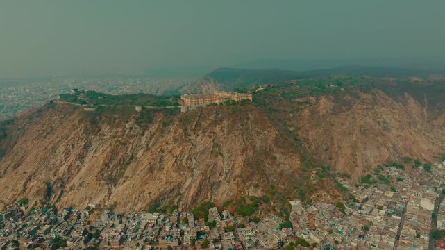 Aerial view of the Nahargarh Fort perched atop a rugged mountain, contrasting with the dense urban sprawl below, Jaipur, Rajasthan, India.