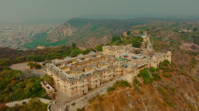 Aerial view of the Nahargarh Fort perched atop the rugged Aravalli Hills, its sandstone walls contrasting with the surrounding green landscape, Jaipur, Rajasthan, India.