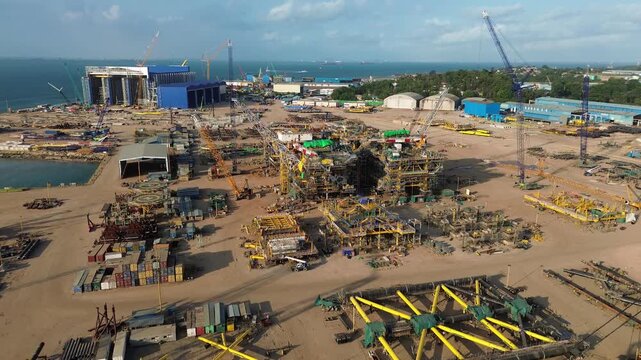 Dynamic aerial panorama of a vast coastal facility engaged in heavy engineering and module fabrication.