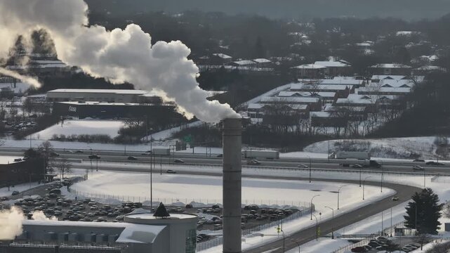 Aerial view of a smokestack emitting smoke, contrasting with the snow-covered landscape and distant buildings, Cincinnati, Ohio, United States.