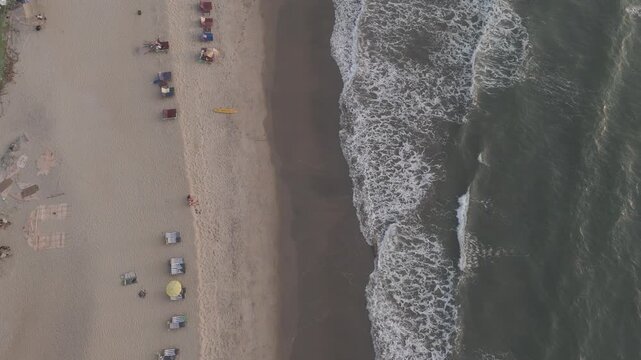 Top-down aerial view of Arambol Beach showing lush greenery, white sand beach, and ocean waves rolling onto the shore on a calm winter evening