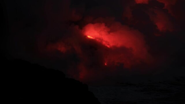 Dramatic volcanic lava flow entering the ocean on the Big Island of Hawaii. Glowing molten lava meets seawater, creating intense steam clouds and fiery red light against a dark coastal landscape.
