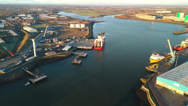 A drone captures Blyth Harbour at dawn with water reflecting sunlight, buildings along the shore, and boats present near the docks