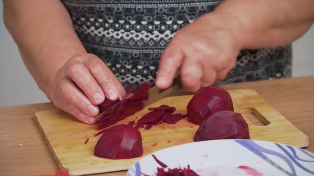 Chopping beetroot into thin slices for cooking Ukrainian borscht. Cutting red vegetable finely for preparing traditional soup. Shredding fresh beet for making borscht recipe. Processing beetroot