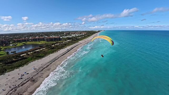Aerial view of a paraglider soaring over the turquoise ocean contrasting with the sandy beach and coastal buildings, Juno Beach, Juno Beach, Florida, United States.