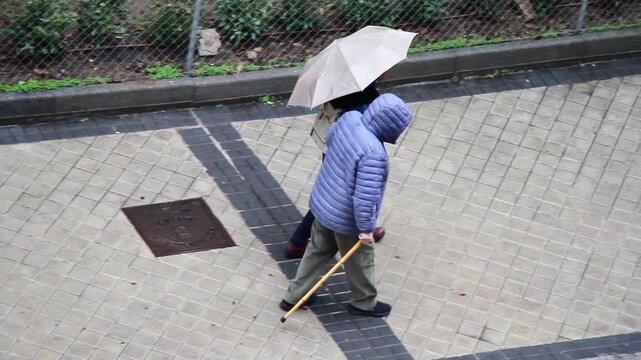Se&ntilde;or mayor y anciano con bast&oacute;n tercera edad y mujer con paraguas paseando en compa&ntilde;&iacute;a en d&iacute;a de lluvia 