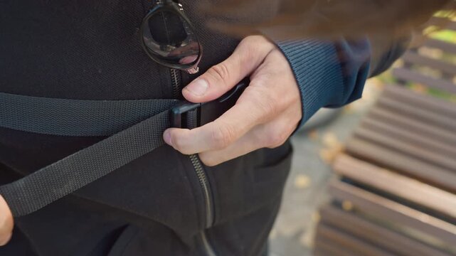 Courier prepares delivery, Man adjusts backpack by park, Male courier securing backpack strap beside autumn leaves, Delivery person adjusting backpack strap with detailed focus near park bench