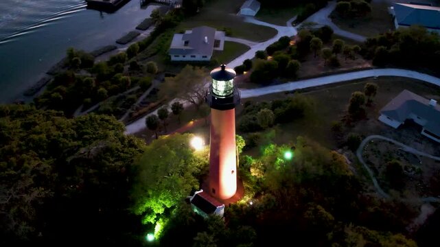 Aerial view of the Jupiter Lighthouse Park with the lighthouse standing tall amidst lush greenery, its beacon shining brightly at dusk, Jupiter, Florida, United States.